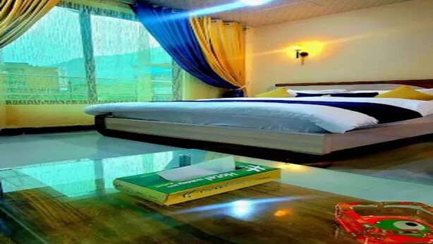 A hotel room with a bed, a glass table, and a window with curtains.