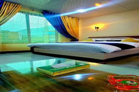 A hotel room with a bed, a glass table, and a window with curtains.