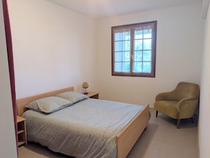 A bedroom with a bed, a chair, a nightstand, a window, and a lamp. - T3 ground floor facing maquis, quiet, close to beaches and mountains (Alata)