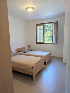 A bedroom with two beds, a window with curtains, a bedside lamp, and a ceiling light. - T3 ground floor facing maquis, quiet, close to beaches and mountains (Alata)