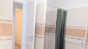 Un baño con ducha, lavamanos y una puerta que da a otra habitación.