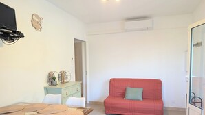 Una sala de estar con un sofá rojo, una mesa de comedor con individuales, un mueble azul claro y un televisor montado en la pared.