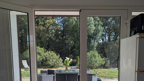 Habitación con puerta corrediza de vidrio que da a un patio exterior con mobiliario de mimbre y un pequeño jardín.