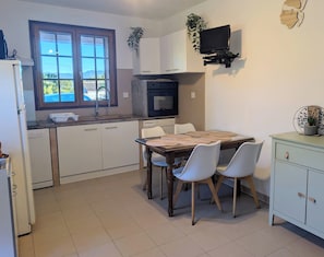 A kitchen with a dining table, chairs, a TV, and a window. - T3 ground floor facing maquis, quiet, close to beaches and mountains (Alata)