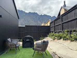 A patio with two wicker chairs, a Weber grill, and a view of mountains. - Stylish Alpine Winter Retreat • Large, Warm, Modern & Peaceful (Jack's Point)