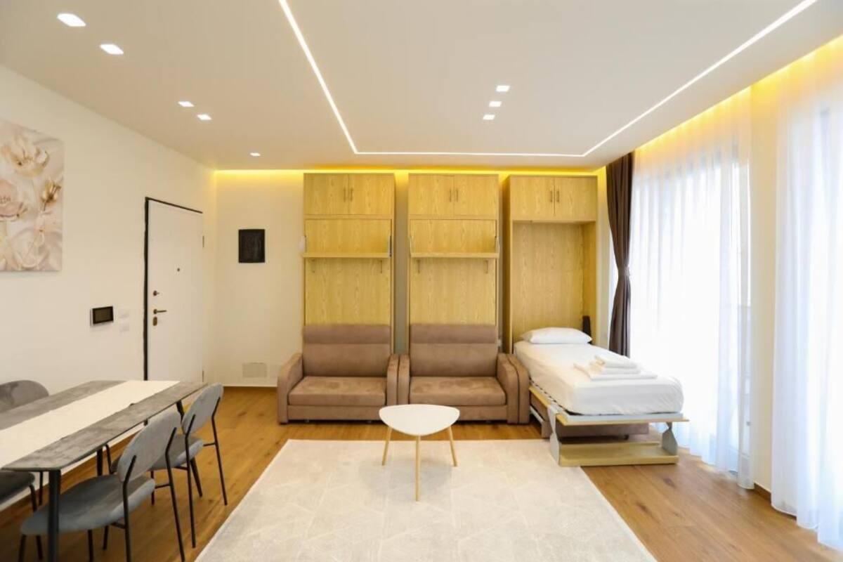 A compact room with a bed, a sofa, a dining table, and a small white table.