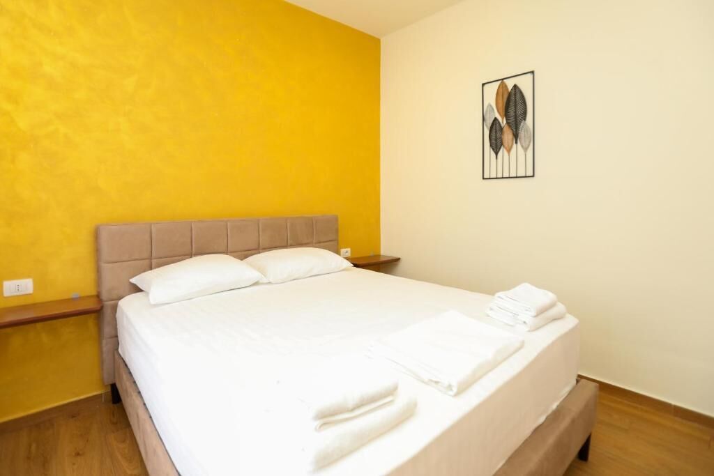 A hotel room with a bed, a nightstand, a wall art piece, and a wooden floor.