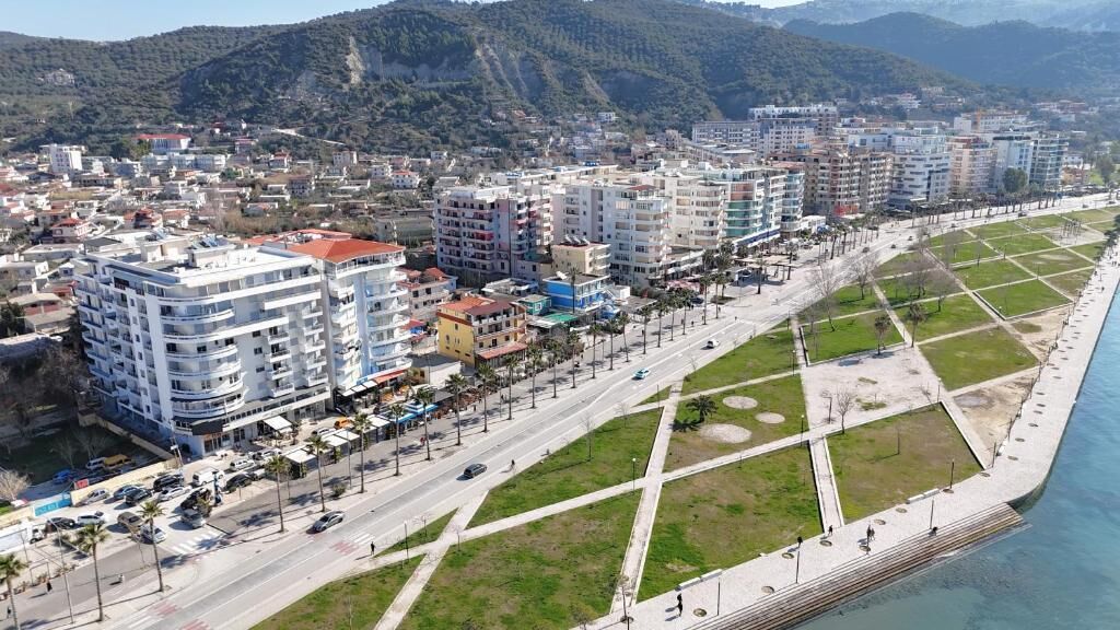 Un paisaje urbano costero con edificios de varios pisos, una avenida amplia y un paseo marítimo.