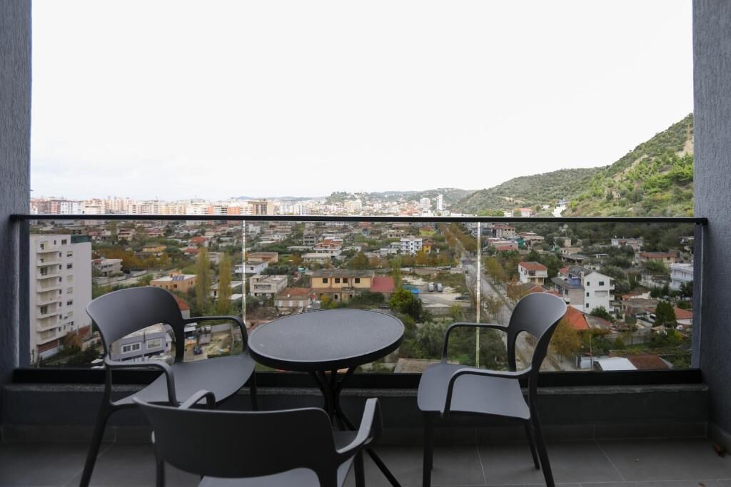 Un balcón con una mesa y sillas, con vistas a un paisaje urbano con edificios y colinas.