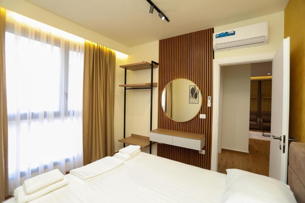 A hotel room with a bed, a bedside table, a mirror, a wardrobe, and a window with curtains.