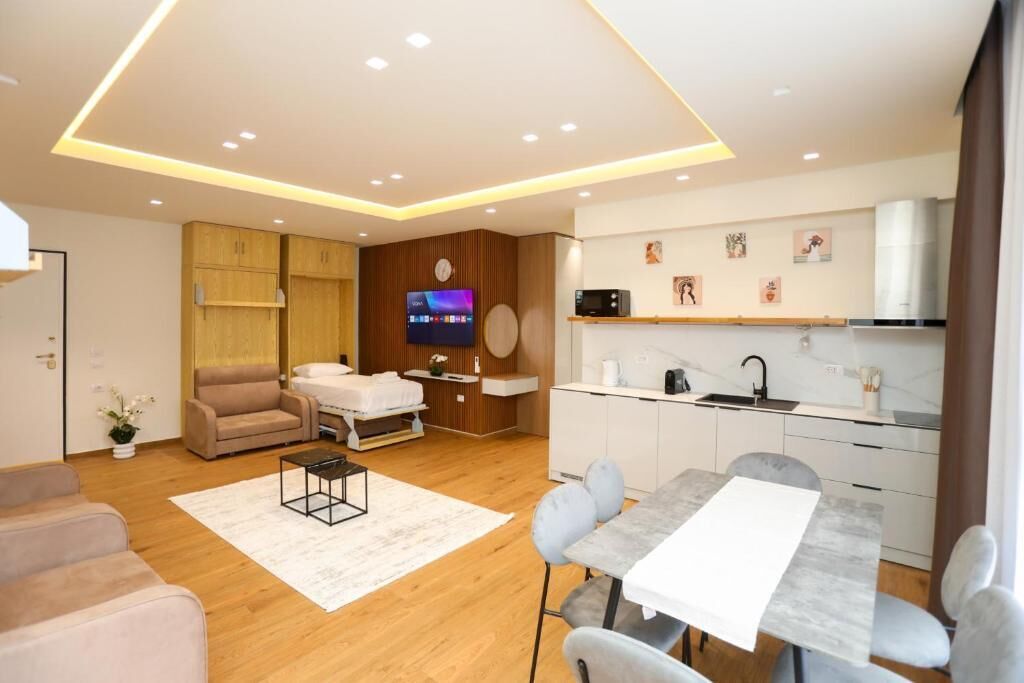 A modern living room with a sofa, a dining table, and a kitchen area with cabinets and a TV.