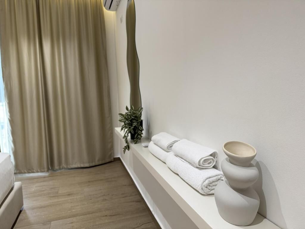 A bathroom with a bathtub, a towel rack with towels, a plant, and a wall-mounted mirror.