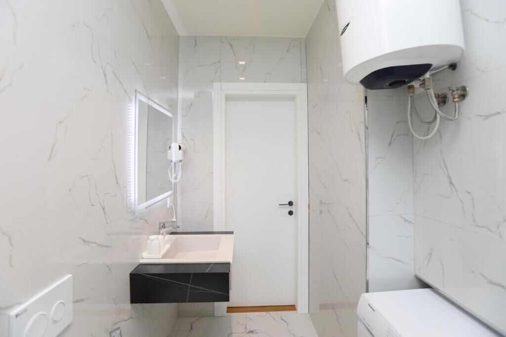 A bathroom with a white sink, a mirror, a white toilet, and a white water heater.