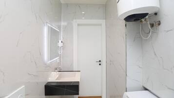 A bathroom with a white sink, a mirror, a white toilet, and a white water heater.
