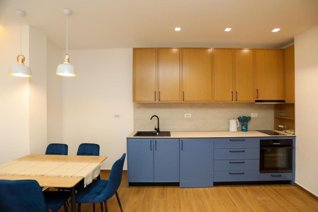 A compact kitchen with wooden cabinets, a sink, and a built-in oven. There is a dining table with chairs and pendant lighting.