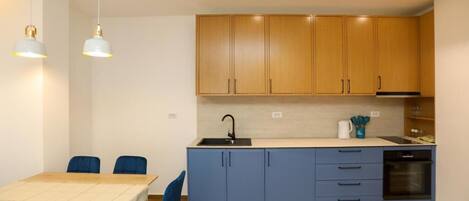 A compact kitchen with wooden cabinets, a sink, and a built-in oven. There is a dining table with chairs and pendant lighting.