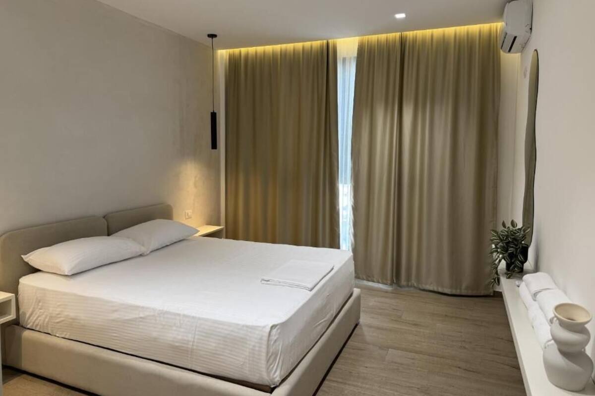 A modern bedroom with a bed, bedside table, curtains, and a small plant.