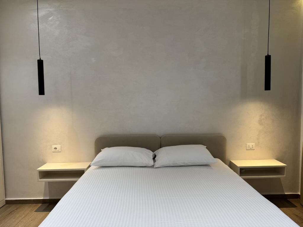 Un dormitorio con cama, dos mesitas de noche e iluminación colgante.