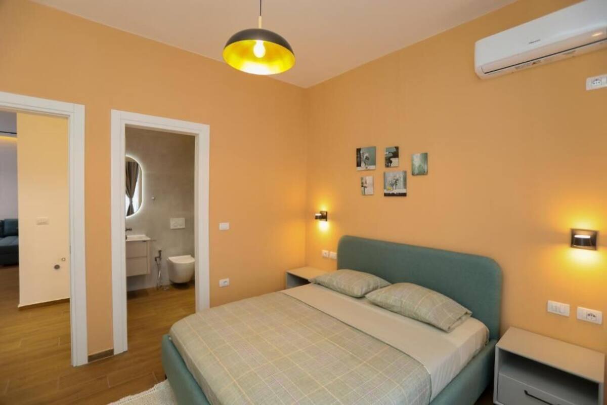 A bedroom with a bed, bedside tables, a wall-mounted air conditioner, and a door leading to a bathroom.