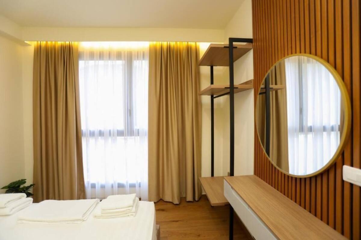 A hotel room with a bed, a desk, a mirror, and a window with curtains.