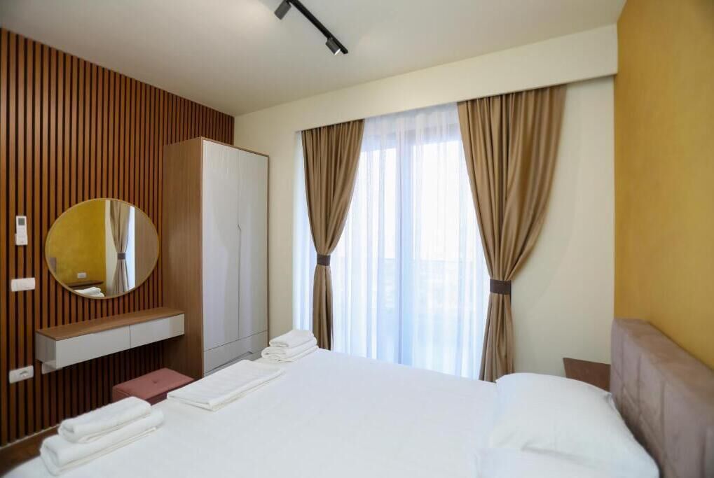 A hotel room with a bed, a wardrobe, a mirror, and a window with curtains.