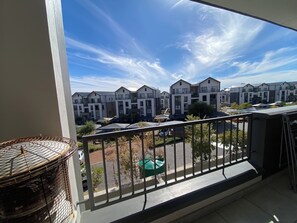 Ein Balkon mit Blick auf moderne Wohngebäude, einem Metallgeländer und einem Korbstuhl.
