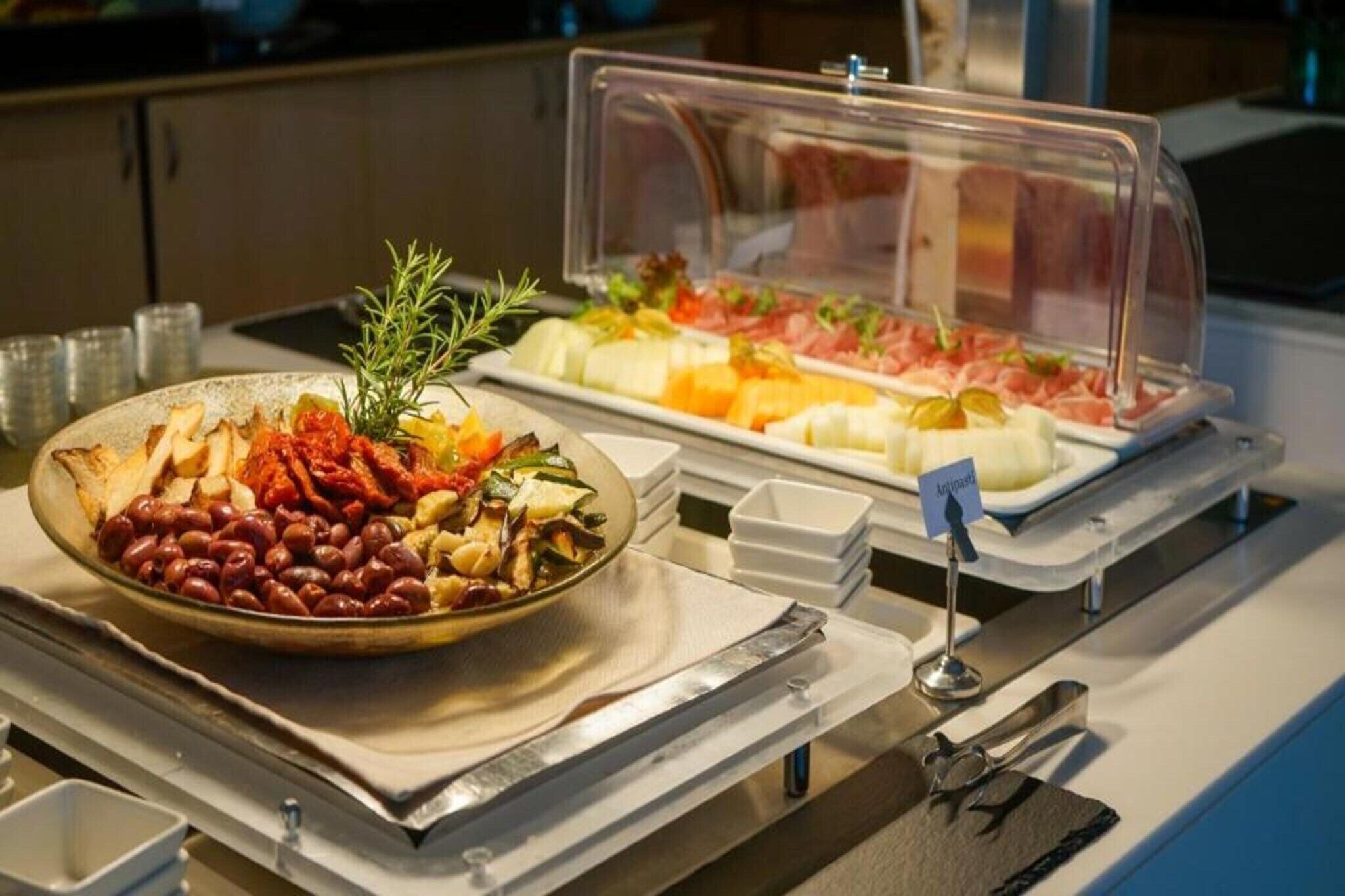 Un buffet proposant une variété de plats, notamment des haricots, des légumes et des viandes, présentés dans des récipients transparents.