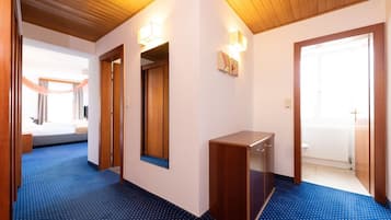A hotel hallway with wooden flooring, a blue carpet, a wooden bench, and a door leading to a bathroom.