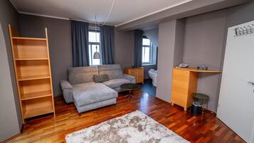 A modern living room with a sofa, a coffee table, a wooden bookshelf, a small side table, and a trash bin.