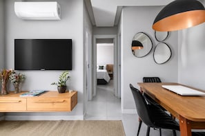 Een moderne hotelkamer met een flatscreen televisie, een houten bureau, een eettafel en een grote spiegel.