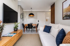 Een moderne woonkamer met een bank, televisie, eettafel, stoelen en een potplant.