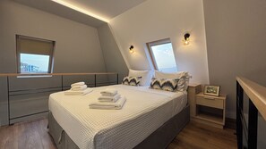 Un dormitorio moderno con una cama, dos lámparas de noche, una mesita de noche, un cuadro enmarcado y una ventana.