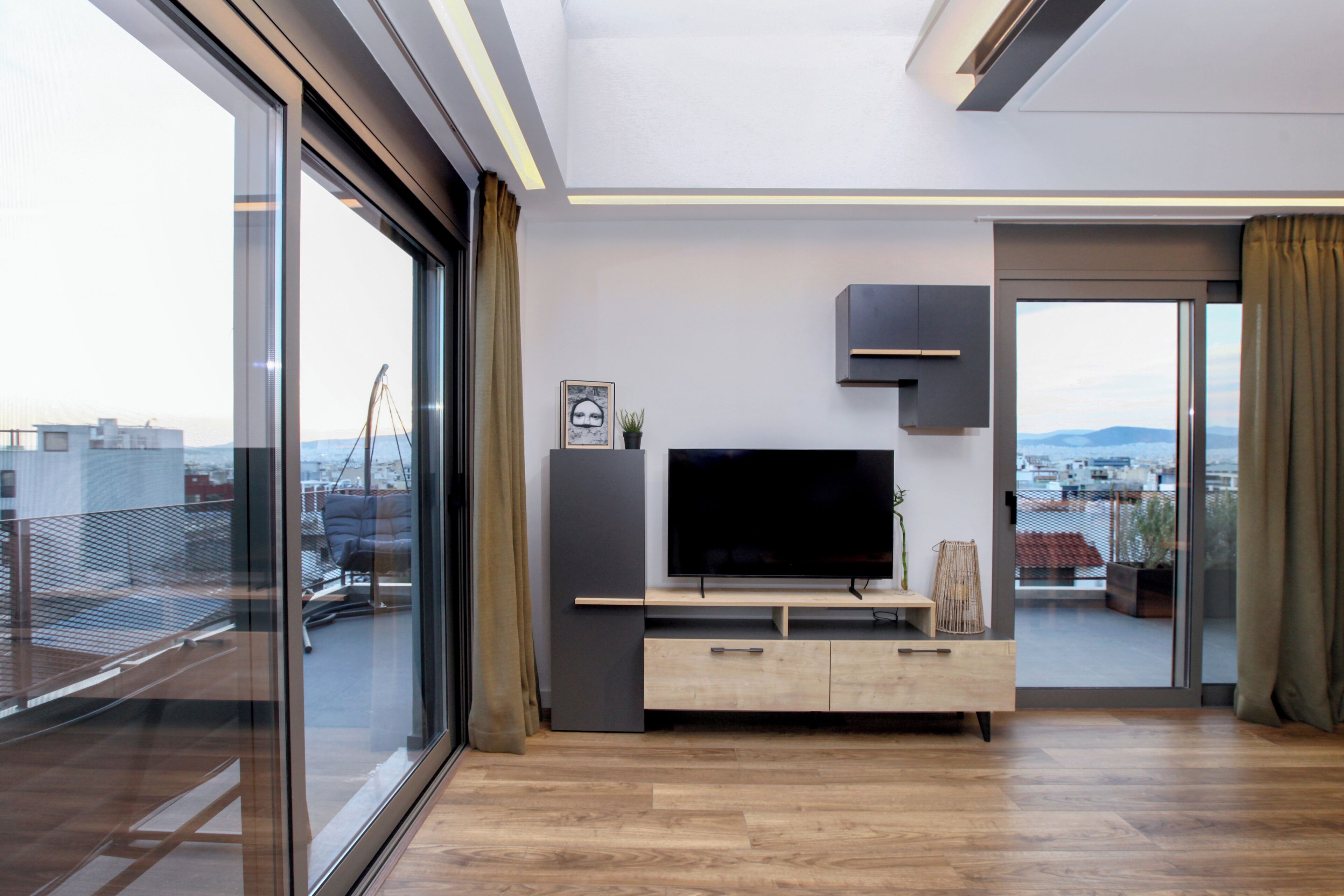 Ein modernes Wohnzimmer mit einem großen Fernseher, Schiebeglasüren und einem Balkon mit Stadtblick.
