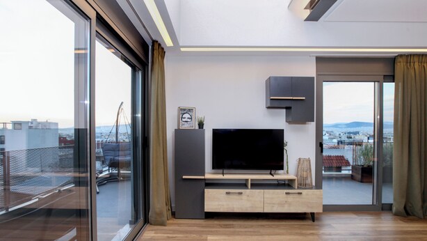 A modern living room with a large TV, sliding glass doors, and a balcony with a city view. - Kirki Luxury Loft (Athina)