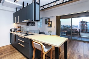 A modern kitchen with a large island, wooden flooring, and a view of the city through large windows. - Kirki Luxury Loft (Athina)
