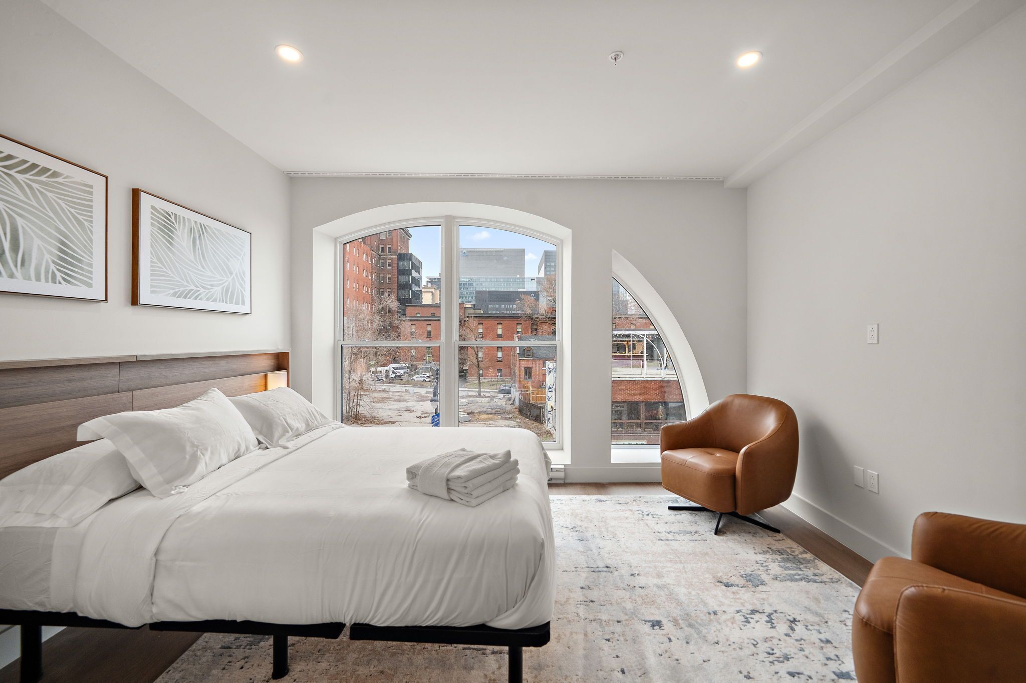 A modern hotel room with a large bed, a seating area, and a view of the cityscape.