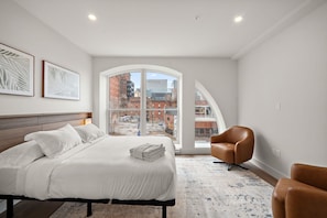 A modern hotel room with a large bed, a seating area, and a view of the cityscape.