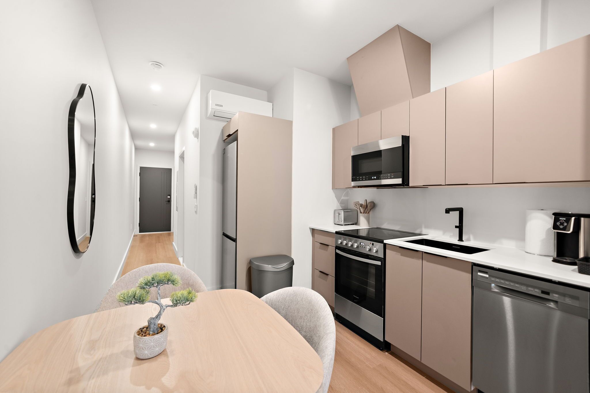 Une cuisine moderne équipée d’appareils électroménagers en acier inoxydable, un coin repas avec une table et des chaises en bois, et une petite plante en pot.