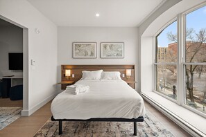 Ein modernes Hotelzimmer mit einem großen Bett, zwei Nachttischlampen, einem Flachbildfernseher und einem großen Fenster mit Blick auf die Stadt.
