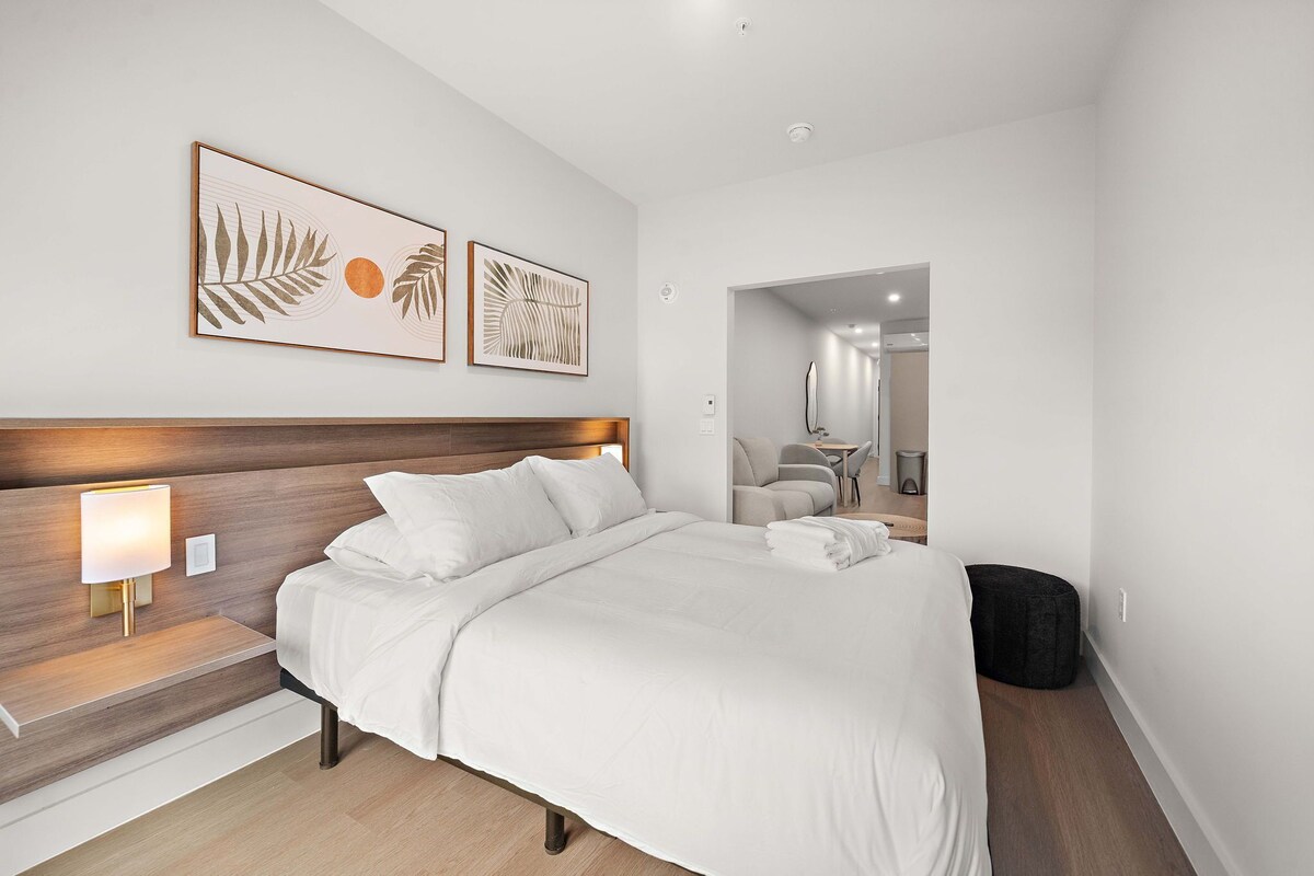Ein modernes Hotelzimmer mit einem großen Bett, einem Holz-Kopfteil, zwei Wandlampen und einem gerahmten Kunstwerk über dem Bett.