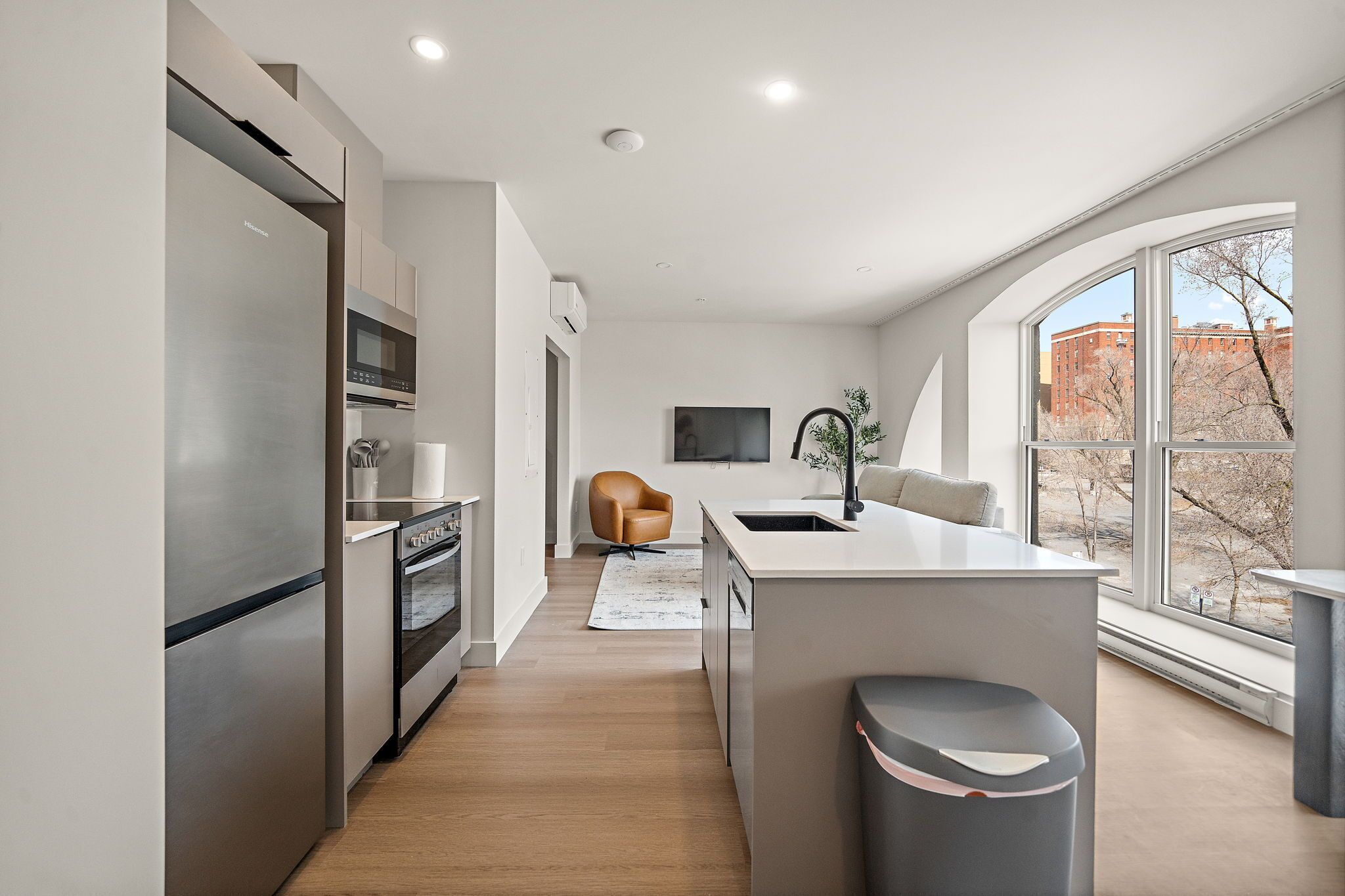 A modern kitchen with stainless steel appliances, a central island, and a large window offering a view of the outside.