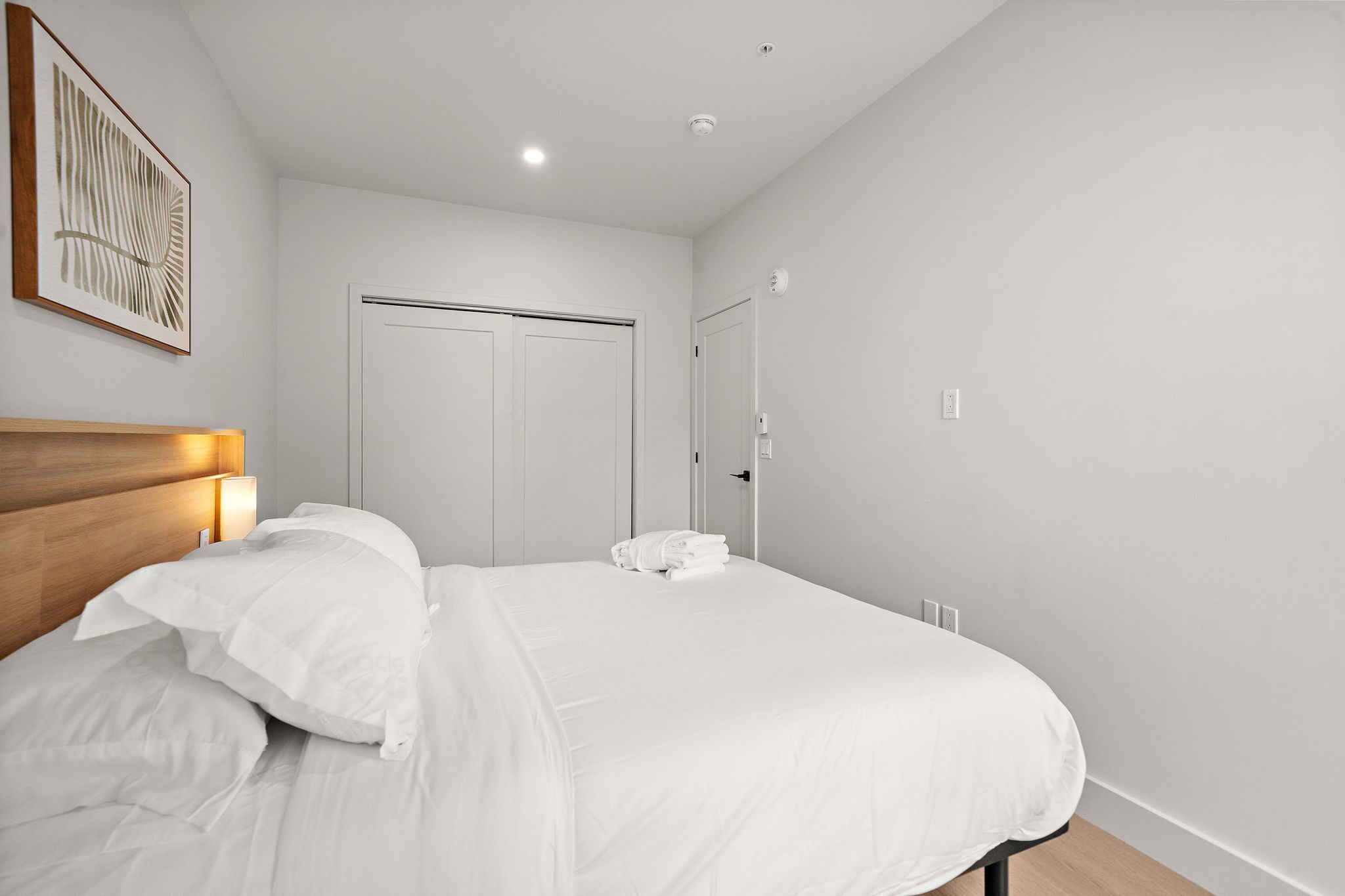 Una camera da letto con un letto, una testiera, un'opera d'arte a parete, una porta e un interruttore della luce.