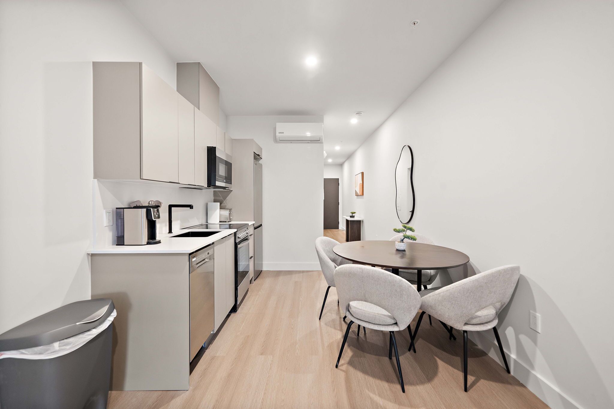 A modern kitchen with white cabinetry, a microwave, and a dishwasher. There is a dining area with a round table and two chairs.