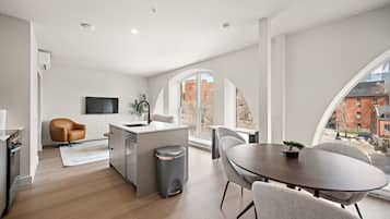 A modern kitchen with a central island, a dining area with a round table, and large windows offering a view of buildings.