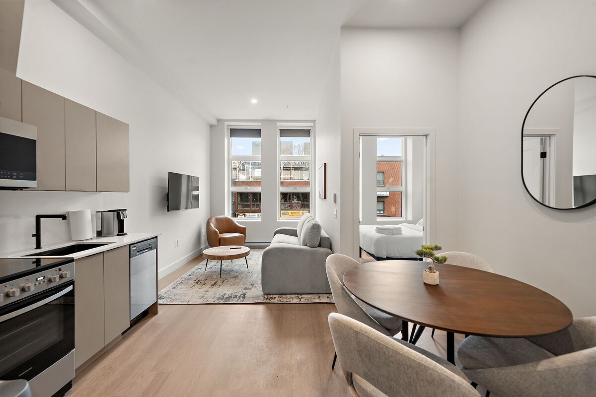 Eine moderne Küche mit Geschirrspüler, Backofen und Flachbildfernseher. Es gibt eine Essecke mit rundem Tisch und Stühlen, und ein Sofa im Wohnzimmer.