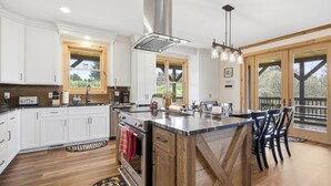 A kitchen with white cabinets, a large island, wooden flooring, and a view of the outdoors. - 5BR Cabin on 3 Acres w Theater, Hot Tub +Fire Pit (Boone)