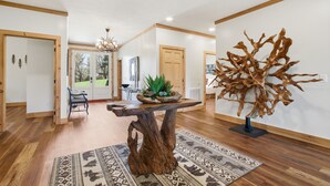 A modern interior with a wooden table centerpiece, a patterned rug, and a large abstract sculpture. - 5BR Cabin on 3 Acres w Theater, Hot Tub +Fire Pit (Boone)