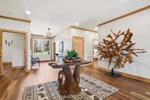 Ein modernes Interieur mit einem Holztisch in der Mitte, einem gemusterten Teppich und einer großen abstrakten Skulptur.