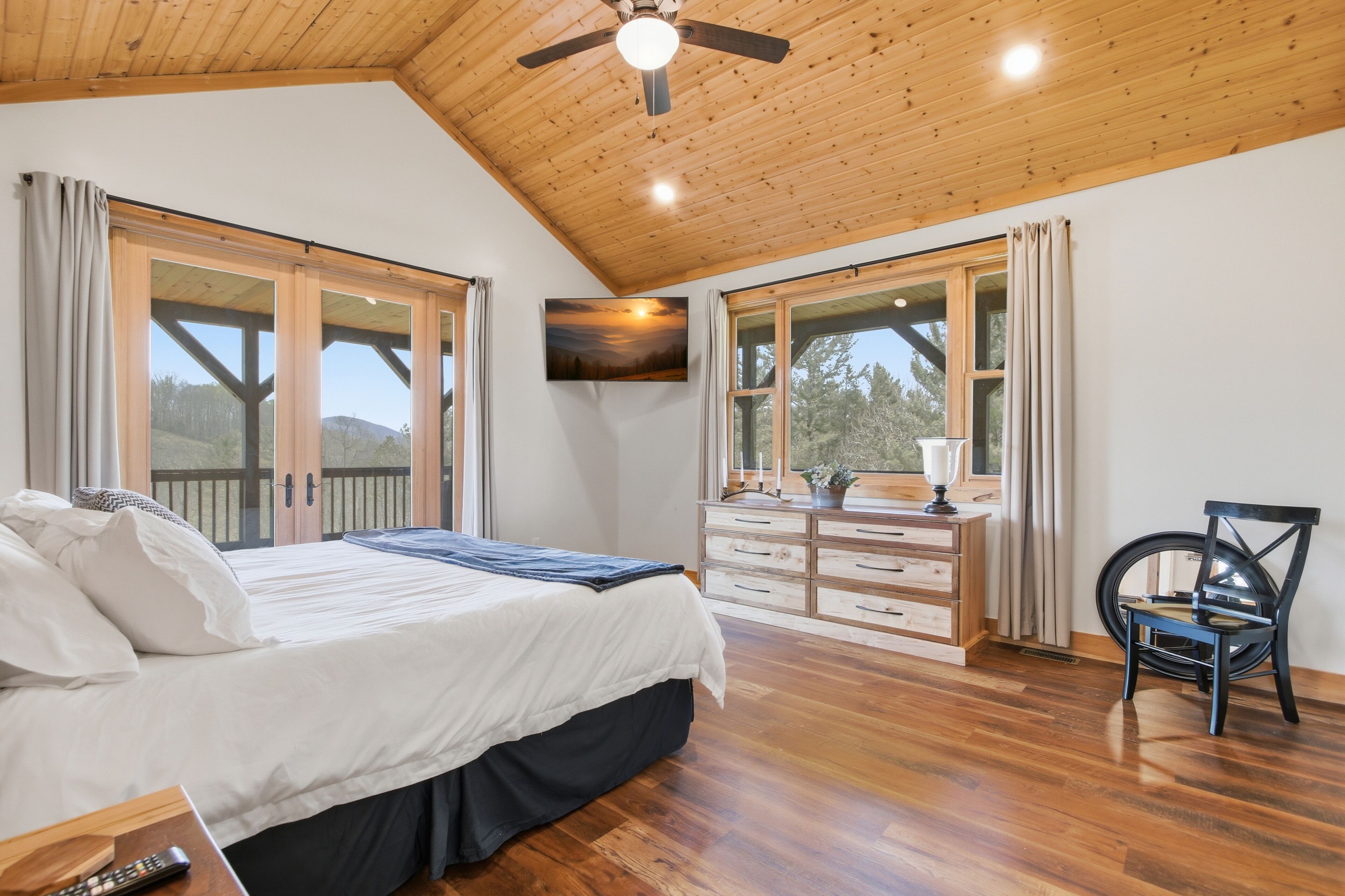 Un dormitorio con cama, cómoda, silla y televisor en la pared.
