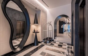 Un couloir moderne avec un grand miroir, une petite table avec une lampe et un chariot.